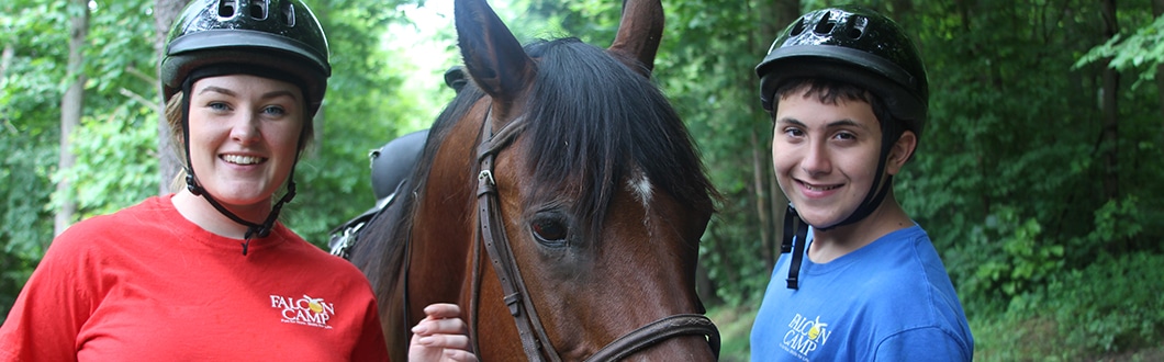 Camp counselor with young boy camper learning how to ride a horse