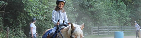 Young girl riding a horse at summer camp