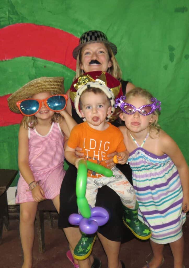 Nici, a woman, sits with her three young children on her lap They are all dressed in silly costumes and making funny faces.