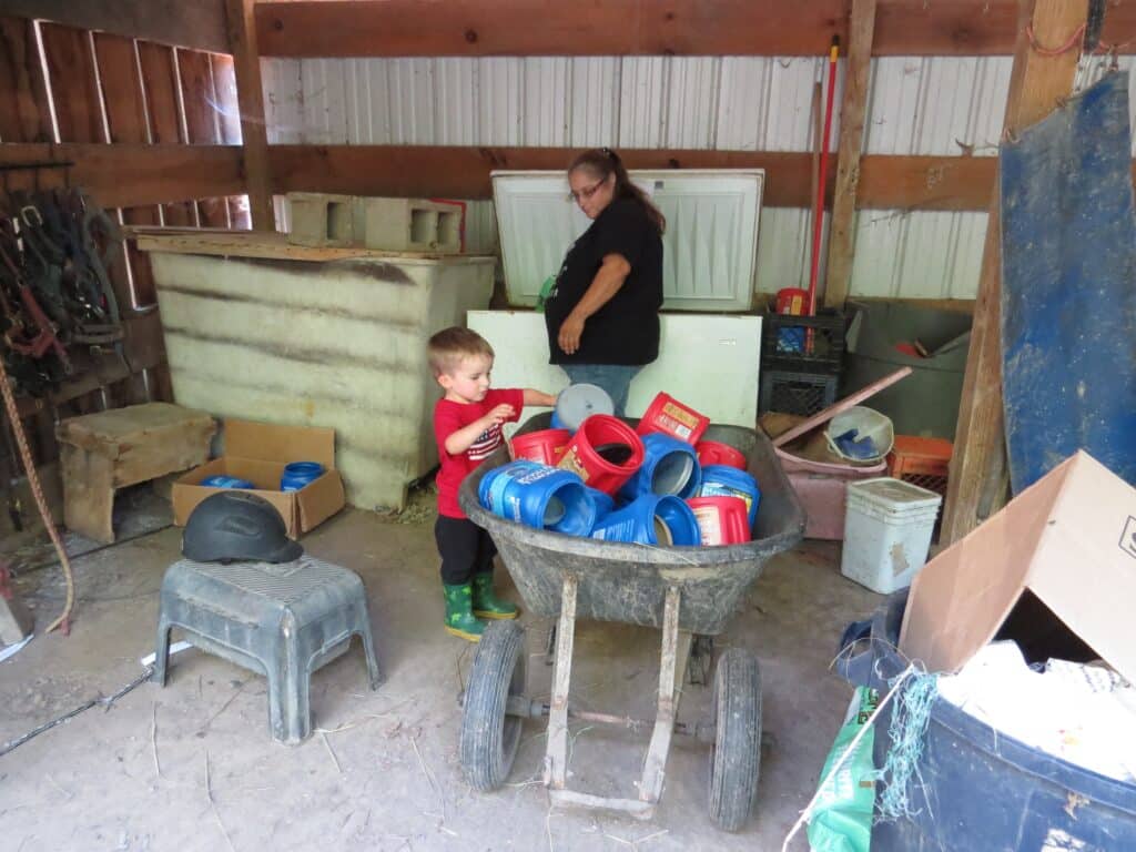Pam, a woman, stands near a wheelbarrow full of empty coffee cans with a small child.