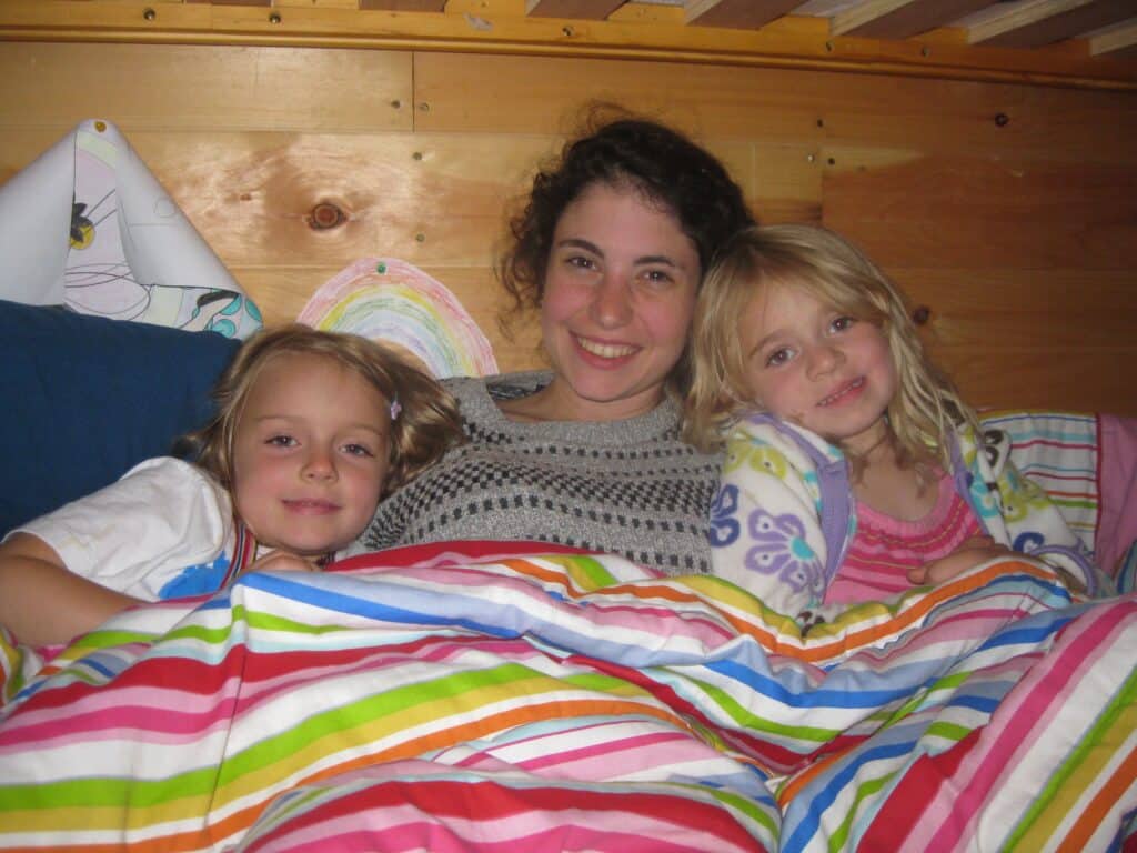 Tali, a woman, sits on a bed with two children. 